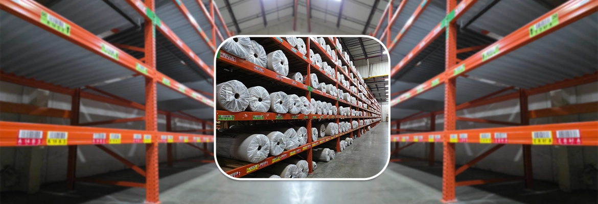 Industrial warehouse featuring heavy-duty orange carpet storage racks fully stocked with wrapped rolls of carpet and flooring materials.